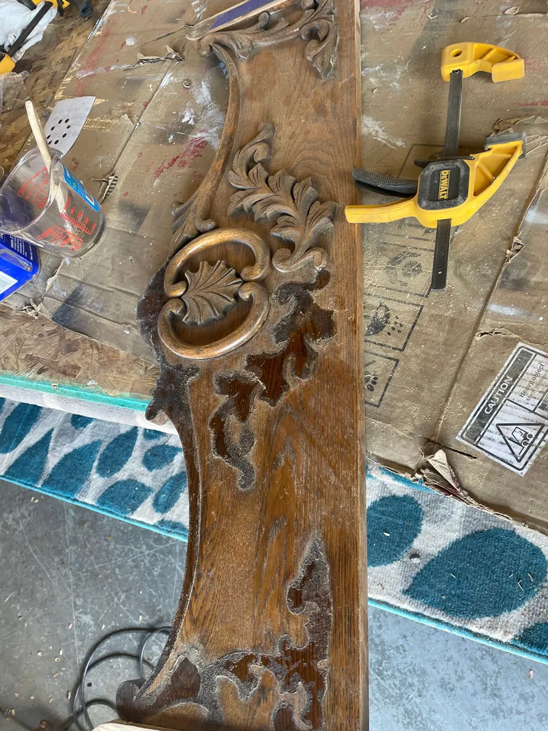 A carved oak panel on the workbench at Sample Studios, its old dark finish partly stripped, a clamp beside it