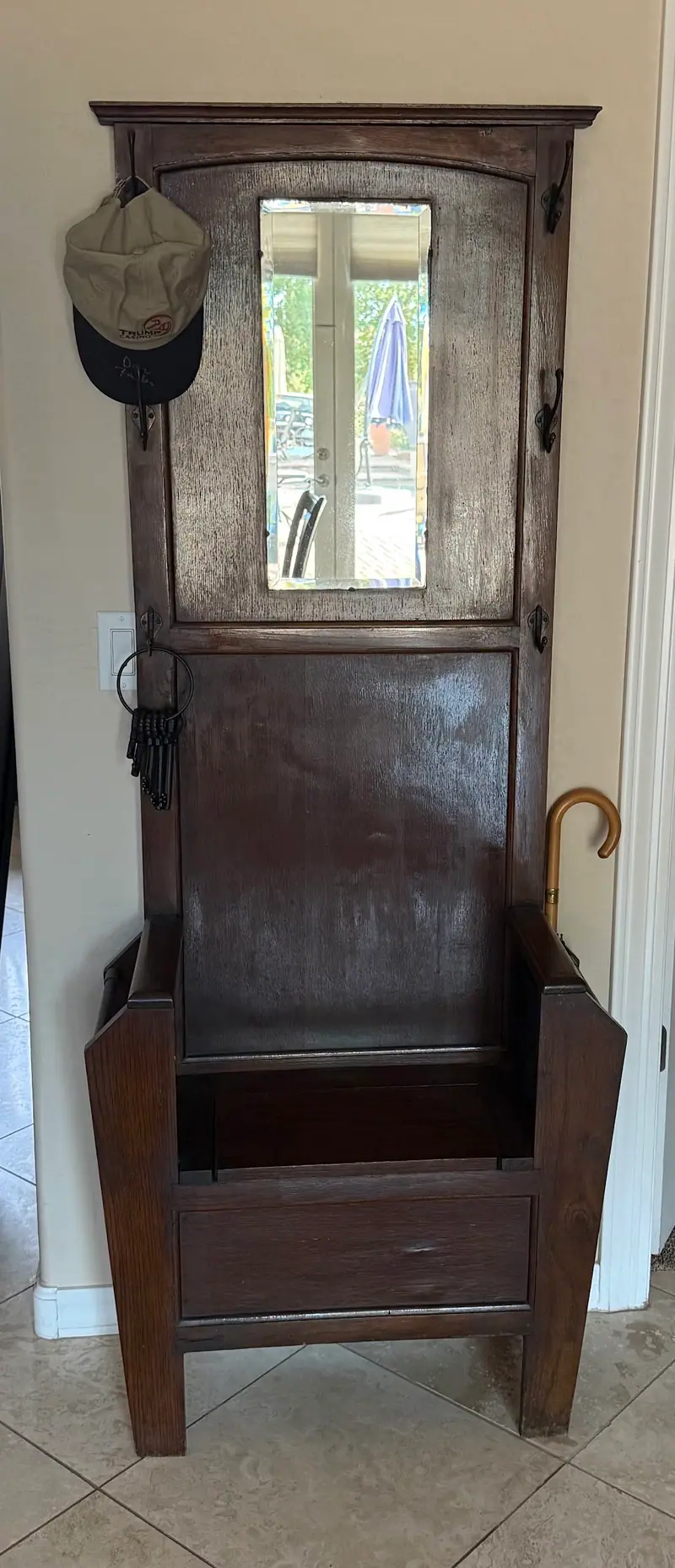 A dark wood hall tree with a mirror, coat hooks and a storage seat
