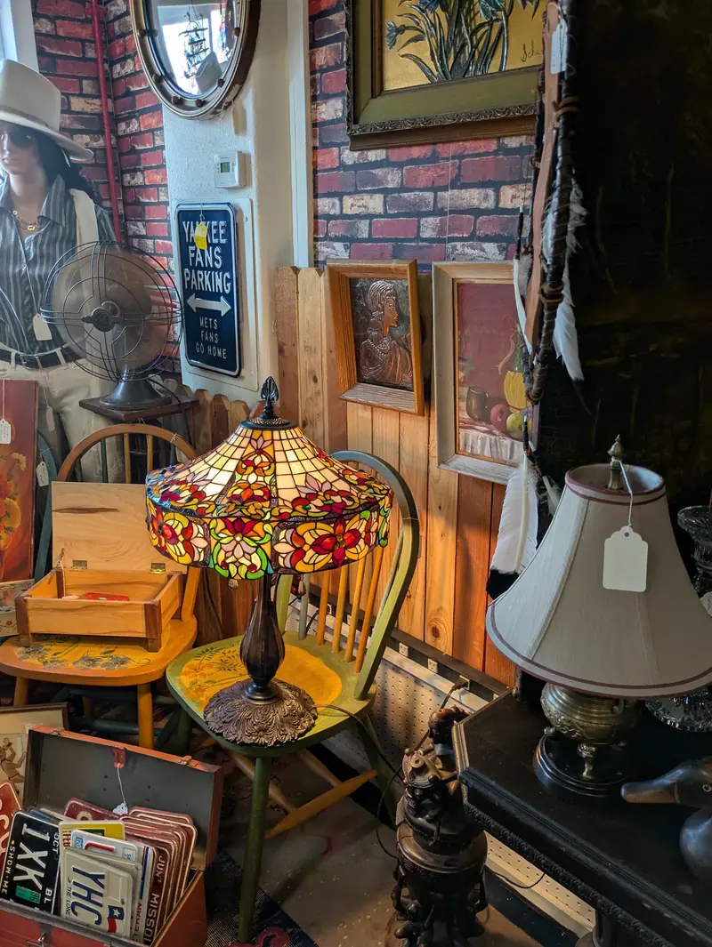 A stained-glass lamp, wooden chairs and framed art in a corner of the store