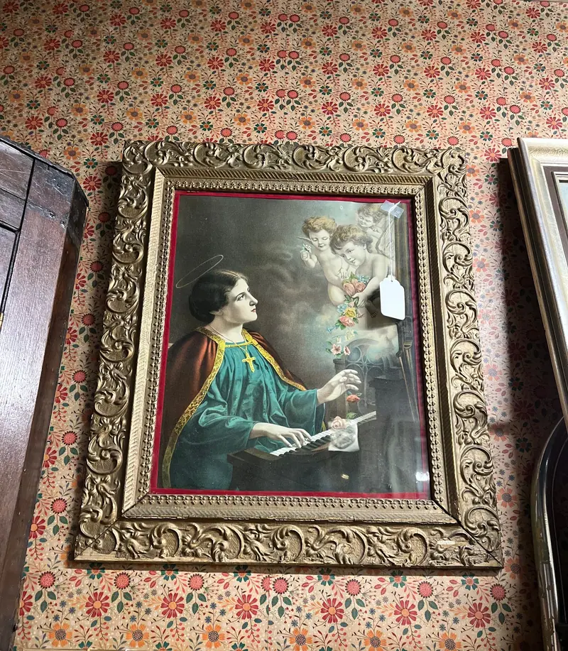 An antique print of a woman writing, in an ornate gilt frame on floral wallpaper