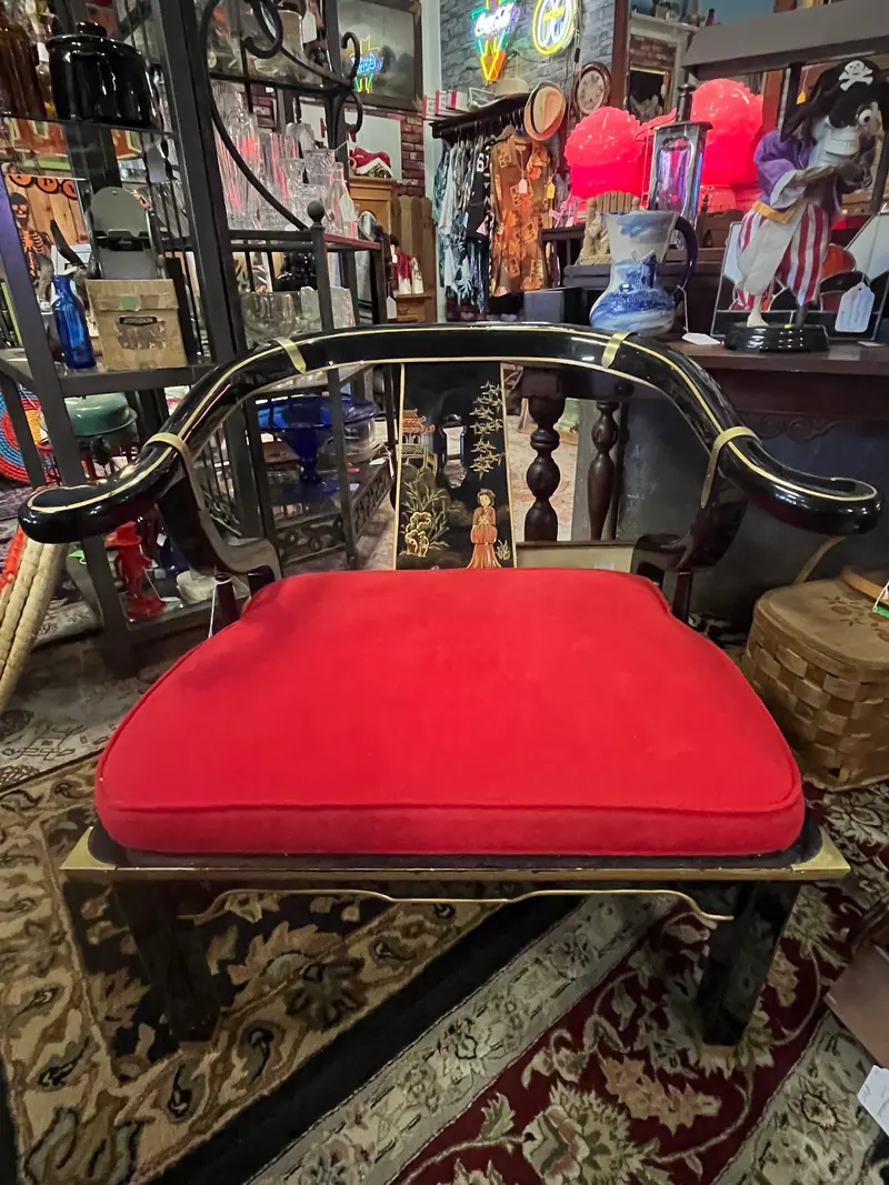 A black lacquered bench with a red cushion among antiques at Sample Studios