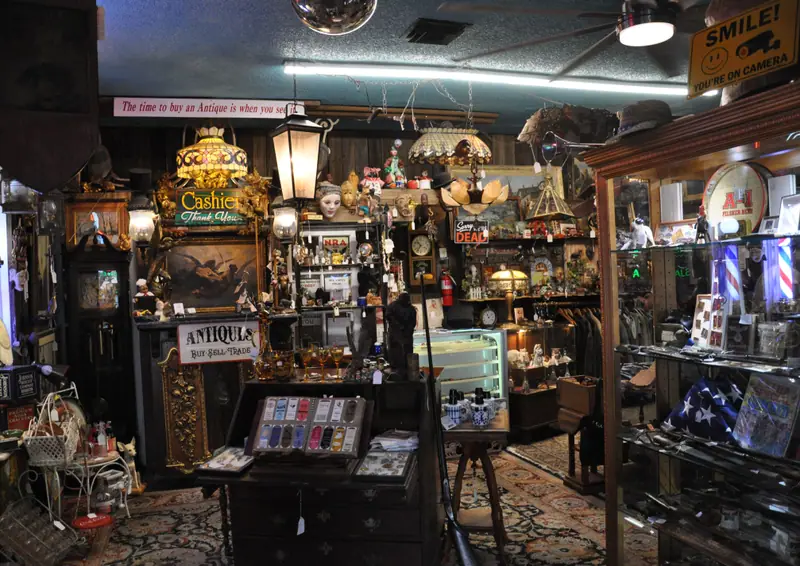 Inside Sample Studios Art & Antiques in Apache Junction: lamps, cabinets, clocks and the Buy, Sell, Trade sign at the counter
